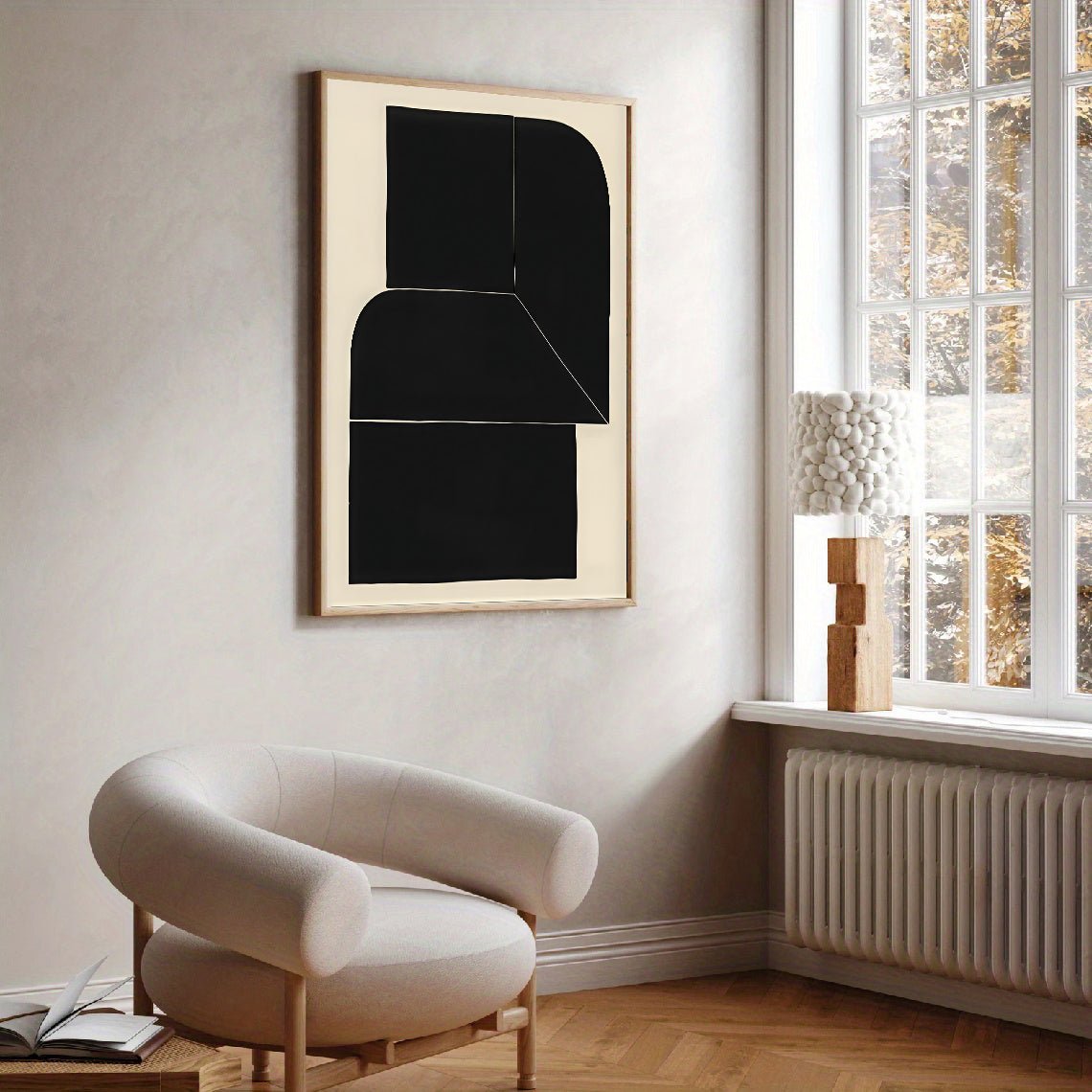 Modern interior with a black abstract painting on a white wall, a beige armchair, and a window with a view of trees.